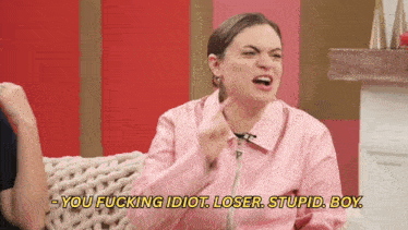 a woman in a pink jacket says " you fucking idiot loser stupid boy " while sitting on a couch