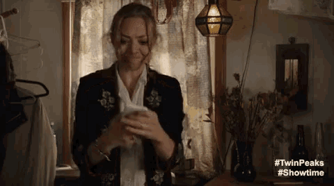 a woman is standing in front of a window holding a cell phone in her hands .