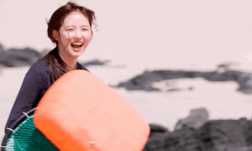a woman is laughing while holding an orange object