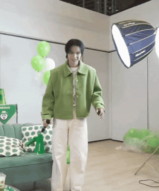 a man in a green jacket stands in front of a green couch with polka dot pillows