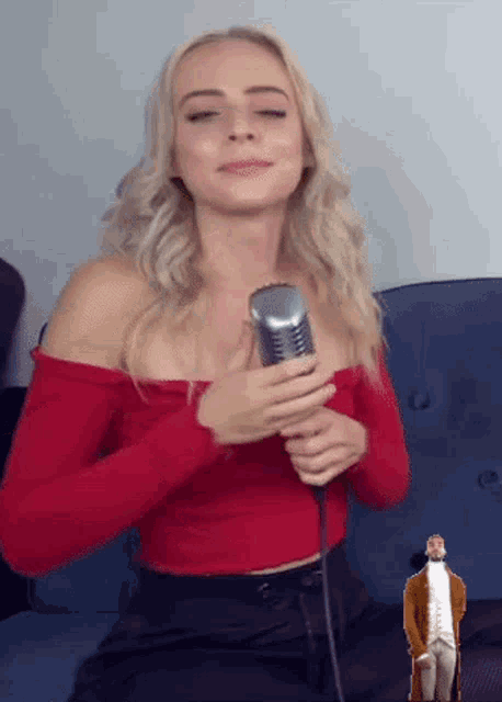 a woman in a red top is singing into a microphone with a man in a brown coat standing behind her