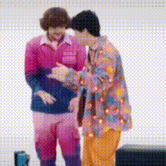 a man in a pink jacket is hugging another man in a colorful jacket