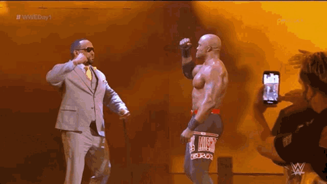 a man in a suit and tie stands next to a man in a wrestling trunks with the word lucha on them