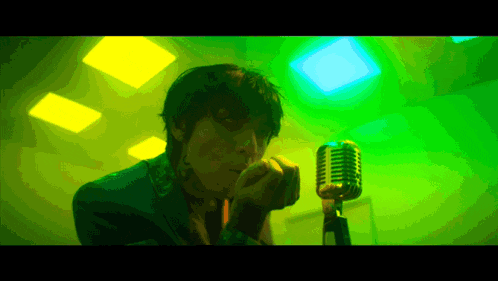 a man singing into a microphone in front of a green background