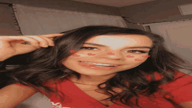 a woman in a red shirt with hearts on her face smiles