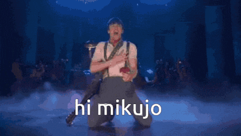 a man is playing a guitar on a stage with the words hi mikujo written on it .