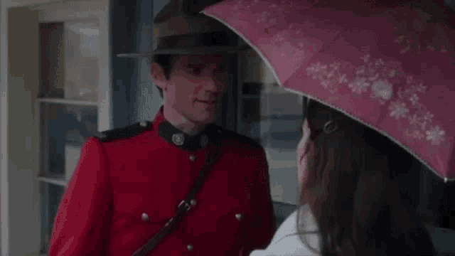 a man in a red uniform is holding a pink umbrella over a woman in a white coat .
