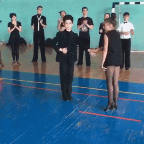 a group of people are dancing on a blue floor in a gym