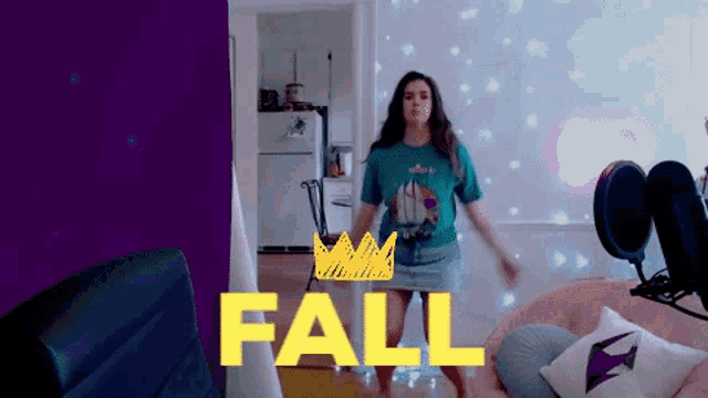 a woman in a blue shirt is dancing in front of a wall that says fall