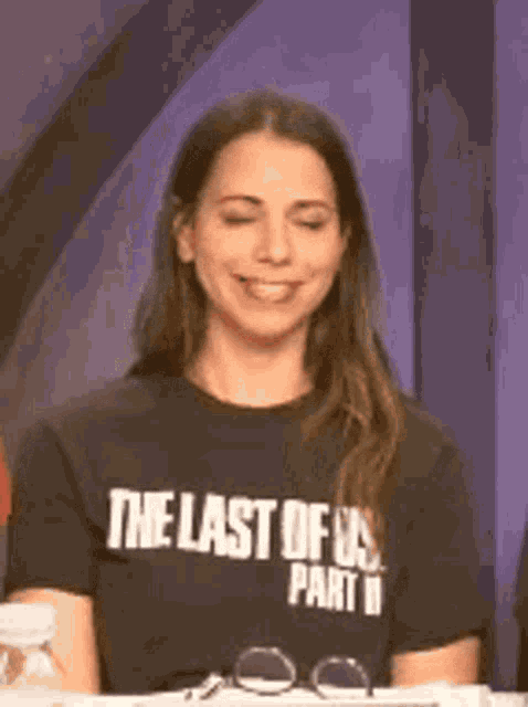 a woman wearing a black t-shirt with the last of us part ii written on it is smiling .