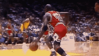 michael jordan is dribbling a basketball on a court in front of a crowd of people .