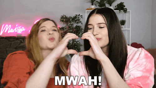 two women are making a heart shape with their hands and the word mwah is on the bottom right