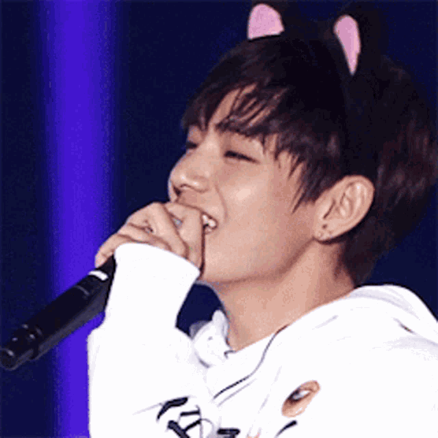 a young man wearing a cat headband is singing into a microphone .