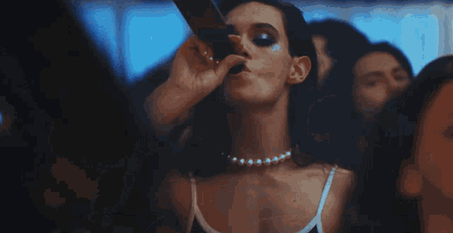 a woman is drinking from a bottle in a crowd