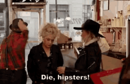 a group of people are standing in a restaurant talking to each other and one of them is saying `` die , hipsters! ''