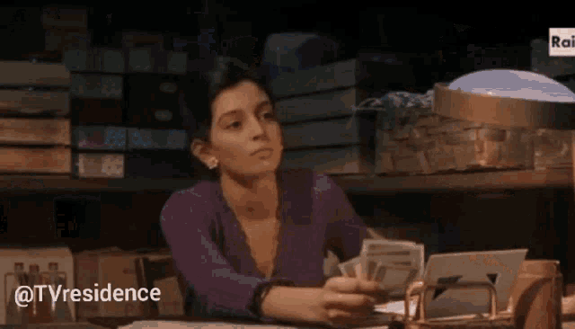a woman in a purple shirt is sitting at a desk holding a bunch of money ..