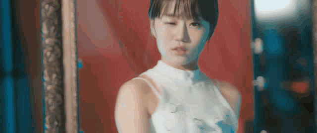 a woman in a white dress is standing in front of a red curtain .