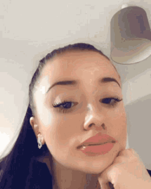 a close up of a woman 's face with her hand on her chin and earrings .
