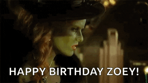 a woman in a witch costume is blowing out a birthday candle and saying `` happy birthday zoey '' .