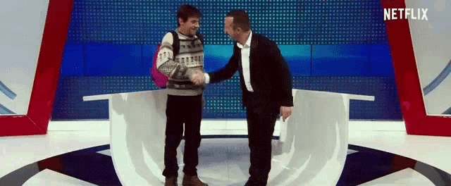 two men shaking hands in front of a screen that says netflix