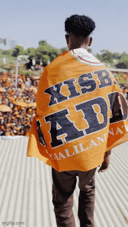 a man wearing an orange shirt that says x isb adi walks in front of a crowd