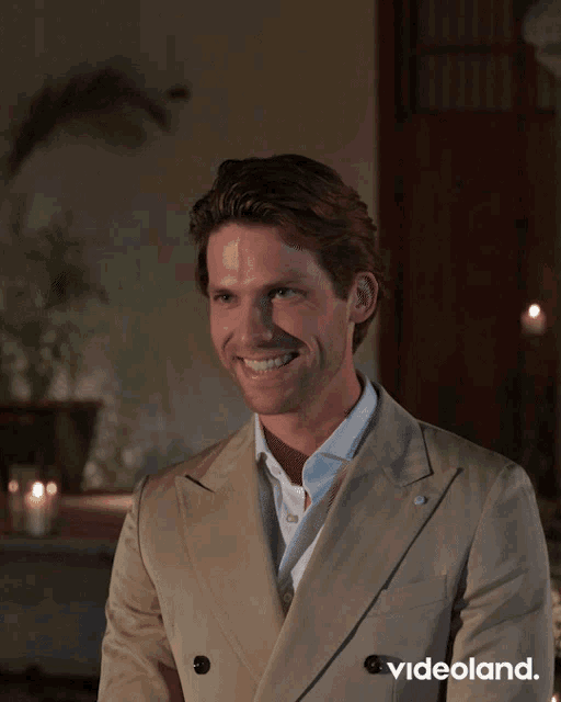 a man in a tan suit is smiling in front of a videoland ad