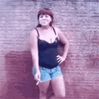 a woman in a black tank top and blue shorts is smoking a cigarette .