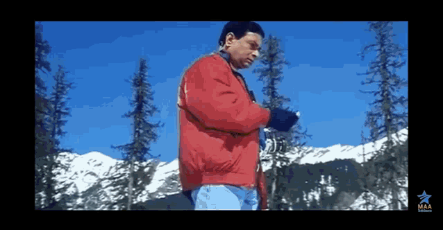 a man in a red jacket is standing in front of a snow covered mountain .