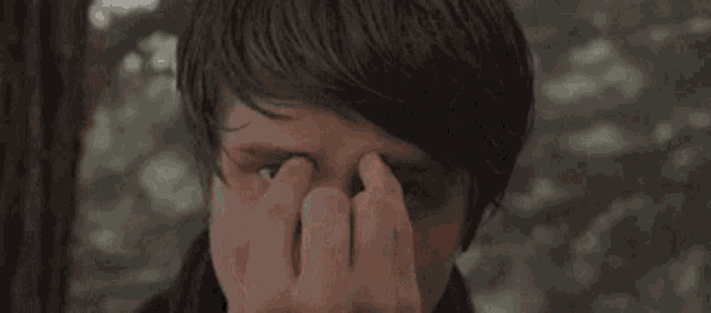a man is rubbing his eyes with his hands while looking at the camera .