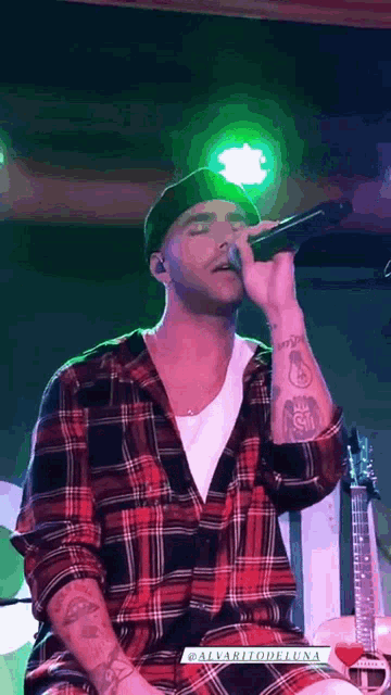 a man in a plaid shirt is singing into a microphone on stage .