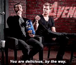 two men are sitting in chairs eating chips with the words you are delicious by the way
