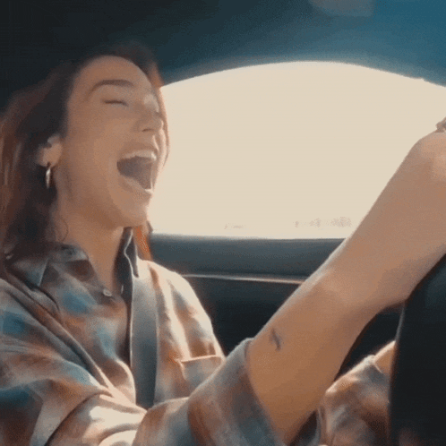 a woman in a plaid shirt is laughing in a car