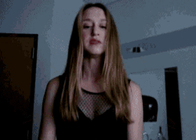 a woman in a black dress is standing in a dark room looking at the camera .