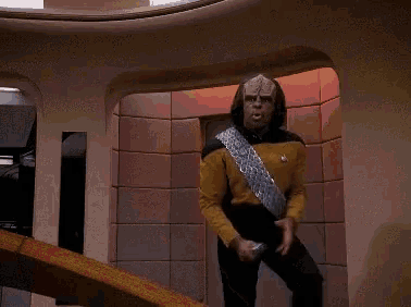 a man in a yellow shirt with a silver sash around his waist is holding a silver object