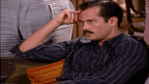 a man with a mustache is sitting in a chair with his hand to his forehead