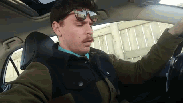 a man wearing sunglasses and a green jacket is driving a car