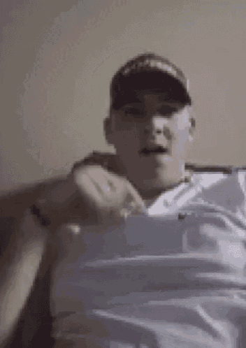 a man wearing a baseball cap and a white shirt is laying on a couch .