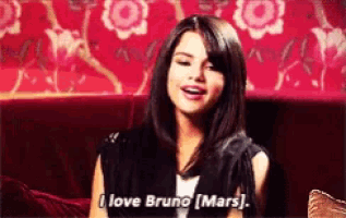 a woman is sitting on a red couch and saying i love bruno mars