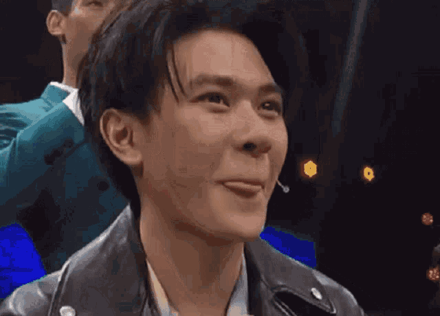 a young man wearing a black leather jacket is making a funny face .