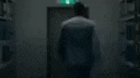 a blurred image of an elevator in a dark room with a green exit sign on the wall .