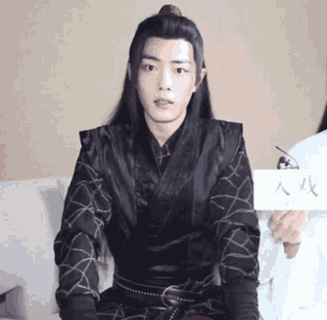 a young man in a black kimono is sitting on a couch holding a sign .