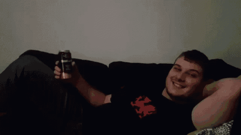 a man laying on a couch holding a beer can