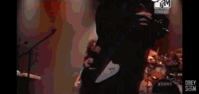 a man is singing into a microphone on a stage with obey system written on the bottom