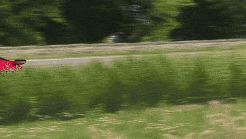a red car is driving down a road next to a field