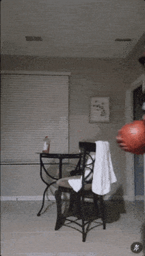 a man holding a basketball in a room with a chair and a table