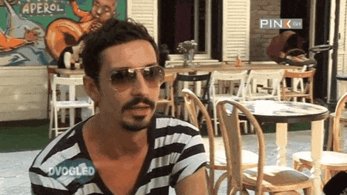 a man wearing sunglasses and a striped shirt with ovogled written on his chest