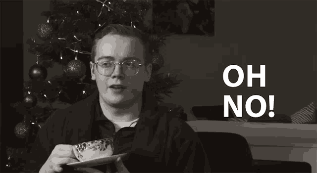 a man with glasses is holding a cup and saucer and says " oh no "