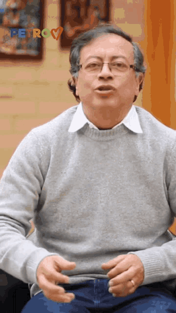 a man wearing glasses and a grey sweater is sitting in front of a petro sign