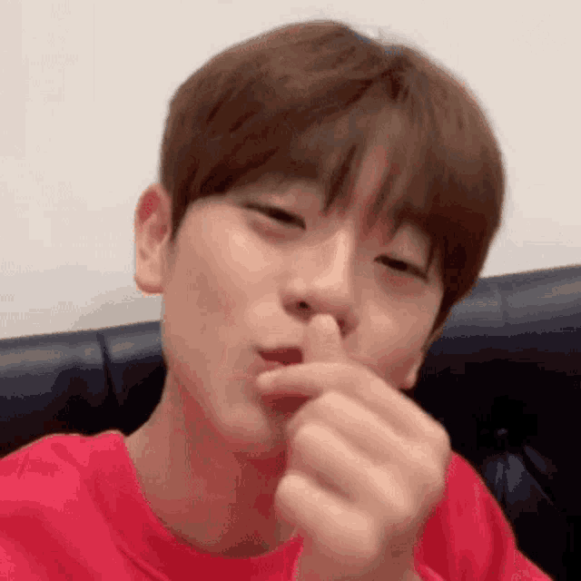 a young man in a red t-shirt is making a heart shape with his finger .
