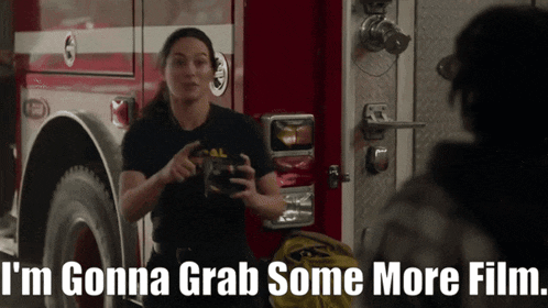 a woman standing in front of a fire truck with the words " i 'm gonna grab some more film " below her